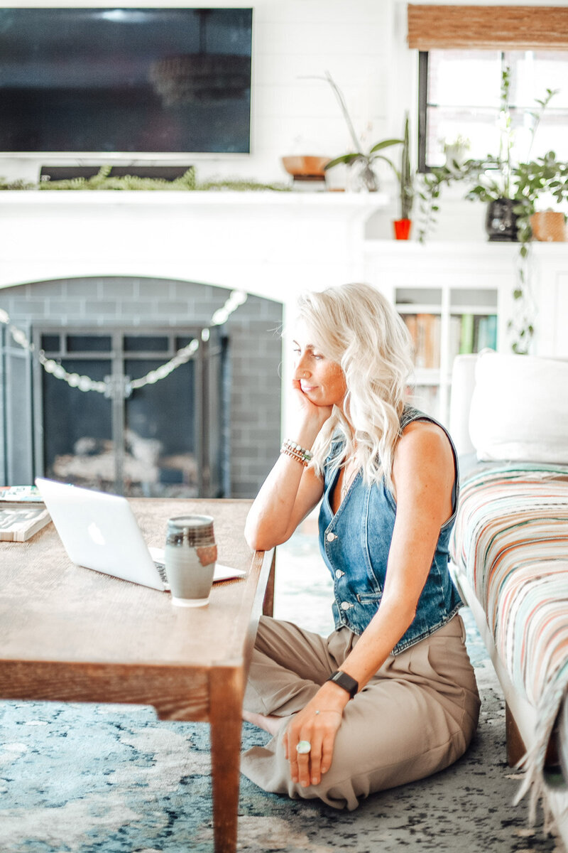 Portland OR realtor Stephanie sits on the floor in her living room looking at her laptop on a coffee table.