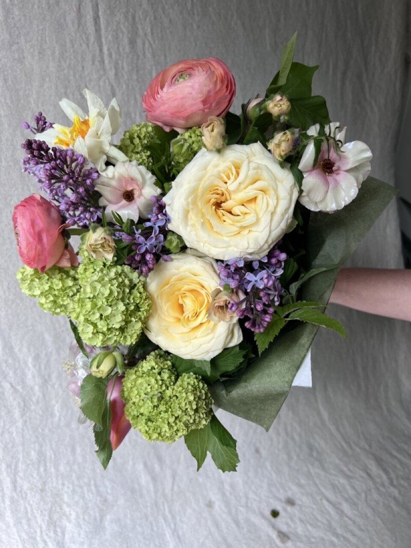 A hand tied spring flower bouquet is held up by a faceless hand, representing Mother's day offerings by Wild Child Flower Co in Eugene.