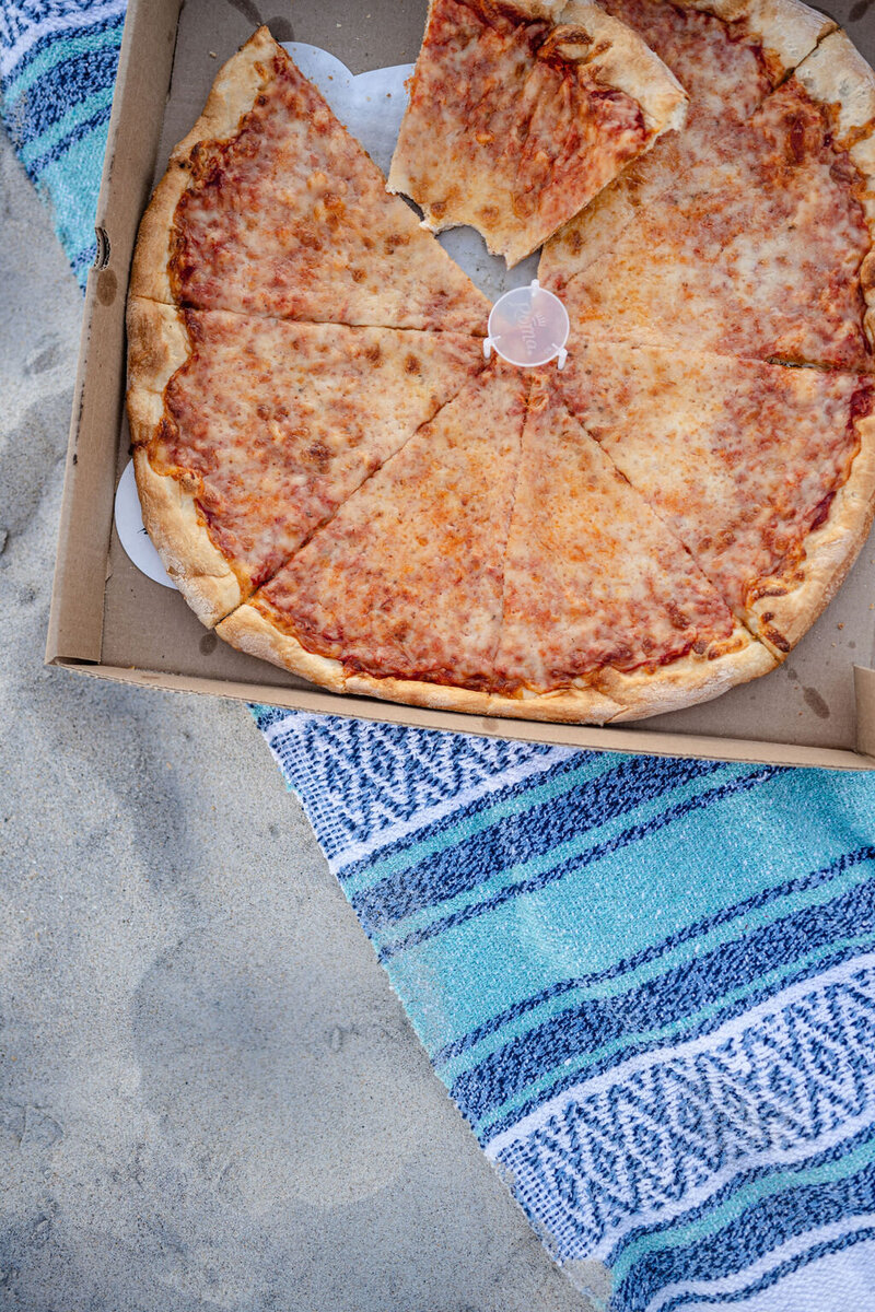 a large pizza sitting on a blue blanket sitting on the beach