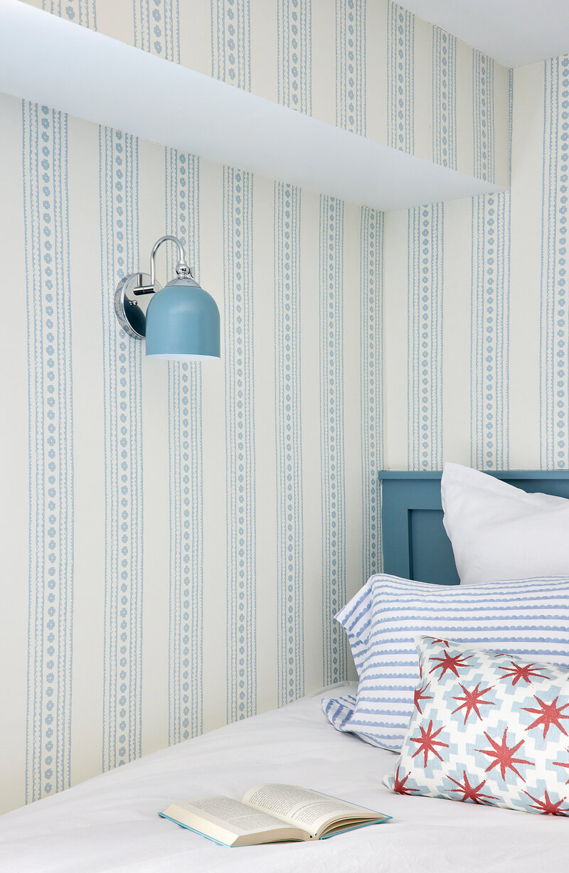 Stylish bedroom featuring blue and white patterned wallpaper, a modern wall-mounted lamp, and a neatly made bed with white and blue bedding