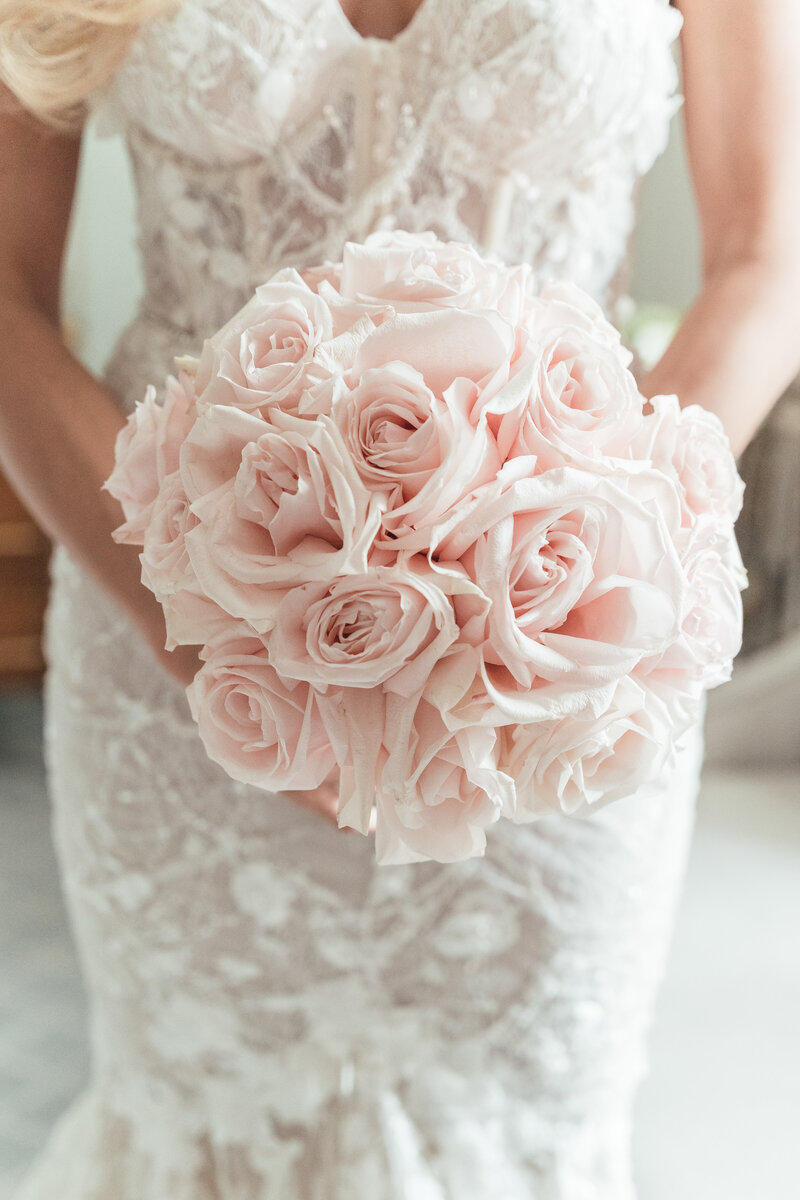 A bride in a blush wedding dress stands with a beautifully rustic bouquet tied with peach silk ribbon.