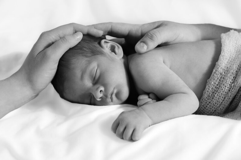 Black and white portrait of a newborn sleeping with a faint smile, wrapped in a knitted wrap. Captured with timeless simplicity by Nostalgia.