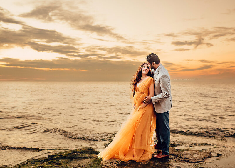 Maternity session captured  on Lake Ontario in oswego with Angel Carter Photographer in Oswego new York wearing yellow dress at sunset