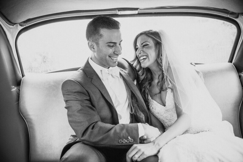 A bride and groom sitting in a car together laughing