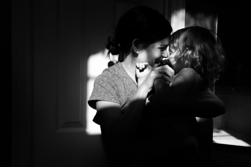 mother holding daughter in shadow touching noses and laughing