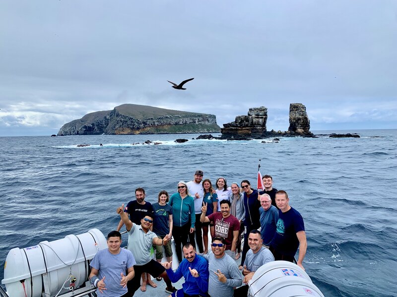 Happy liveaboard diving group poses on deck in front of Galapagos Islands