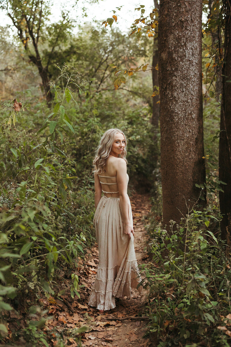 Senior girl walking through a path in the woods wearing a gown. 