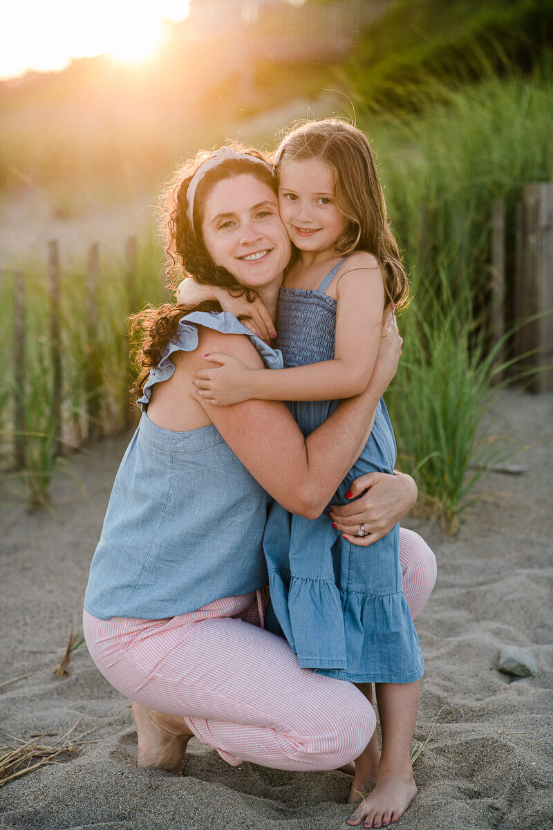 mom and daughter hug on beach ast sunset