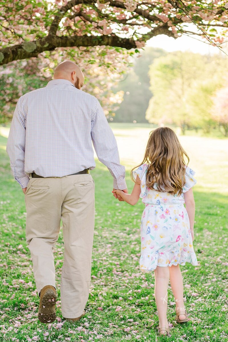 father and daughter holding hands and walking under the cherry blossoms at lancaster central park by york pa photographer