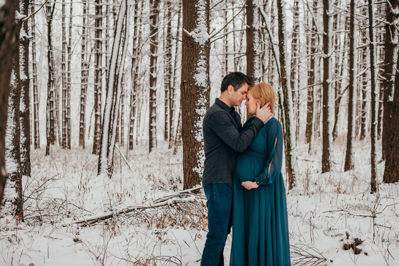 couple snuggling in snow covered winter forest