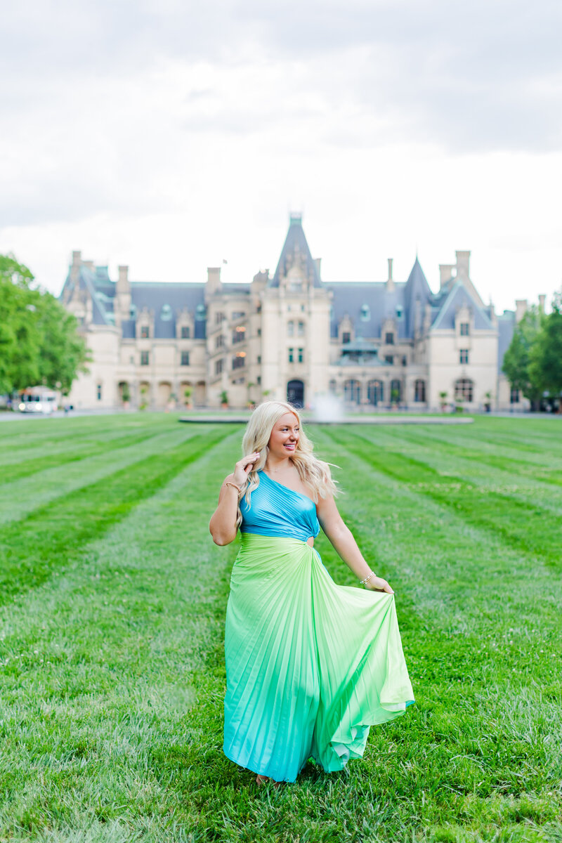 blonde-headed senior in blue and green dressing walking on the front lawn of Biltmore Estate in Asheville, North Carolina