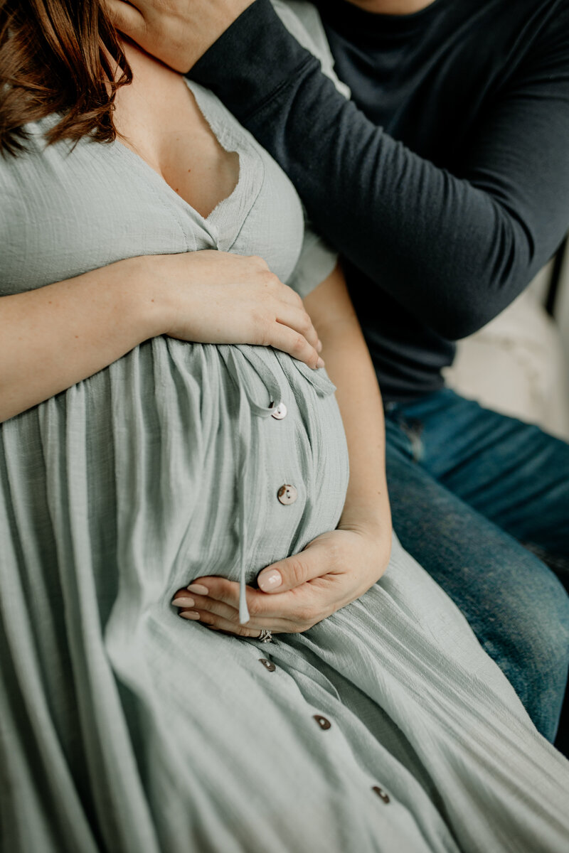 A mom gently holds her belly while her husband lovingly kisses her during a maternity session.
