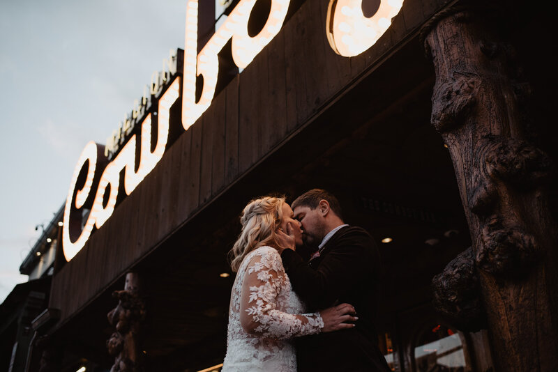 unique weddin gpictures for wyoming elopement with groom kissing his bride under the cowboy bar sign captured by jackson hole photographers
