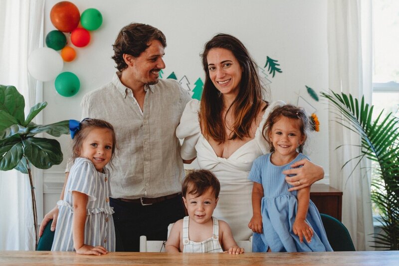 Family of 5 surrounding a one year old boy, celebrating his birthday and smiling at the camera for birthday session