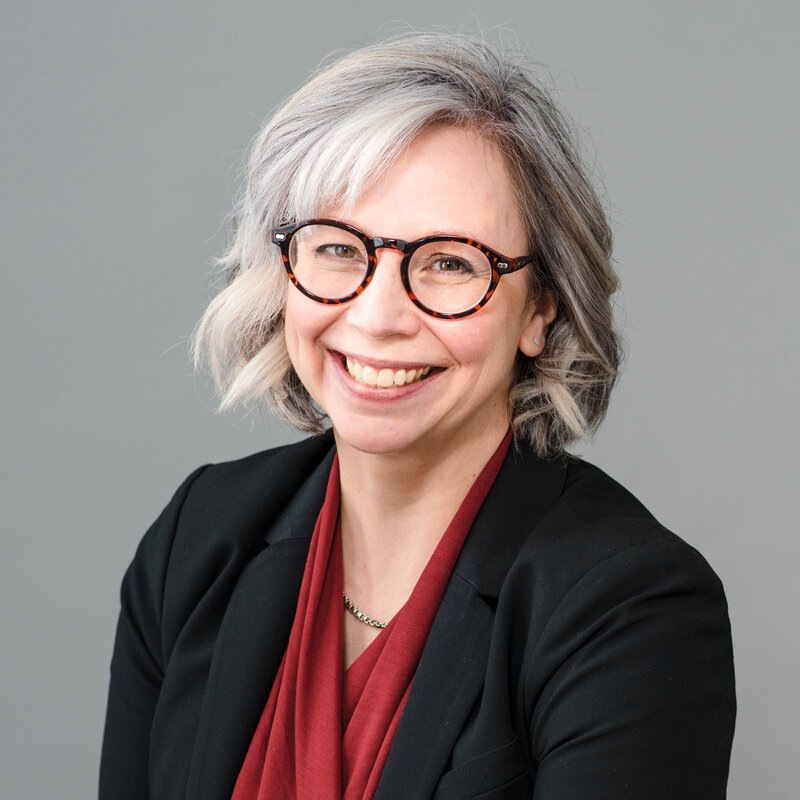 Professional Charlotte headshot photographer captures modern corporate portrait of woman in glasses and blazer against neutral background.