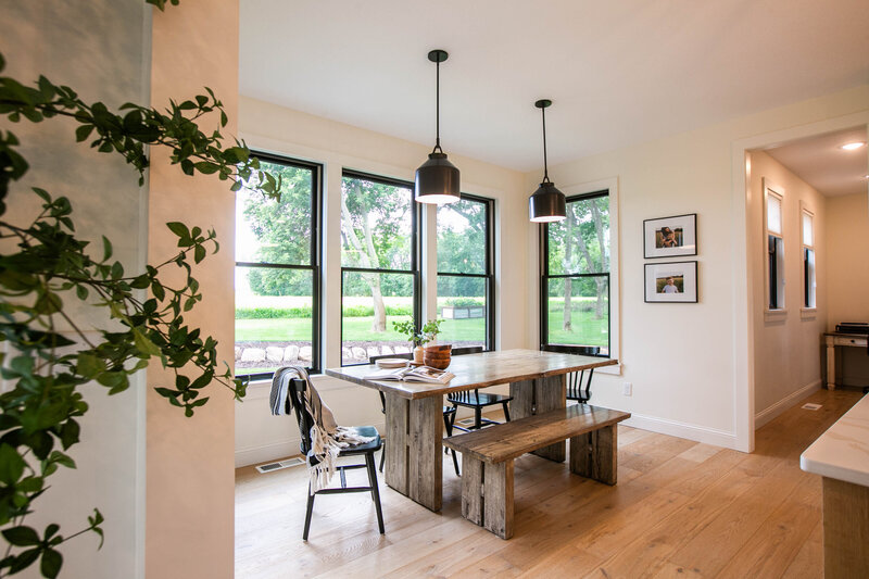 Custom build eat in kitchen with black hanging lights and wood table with bench and white walls designed by Cornerstone Custom Builds