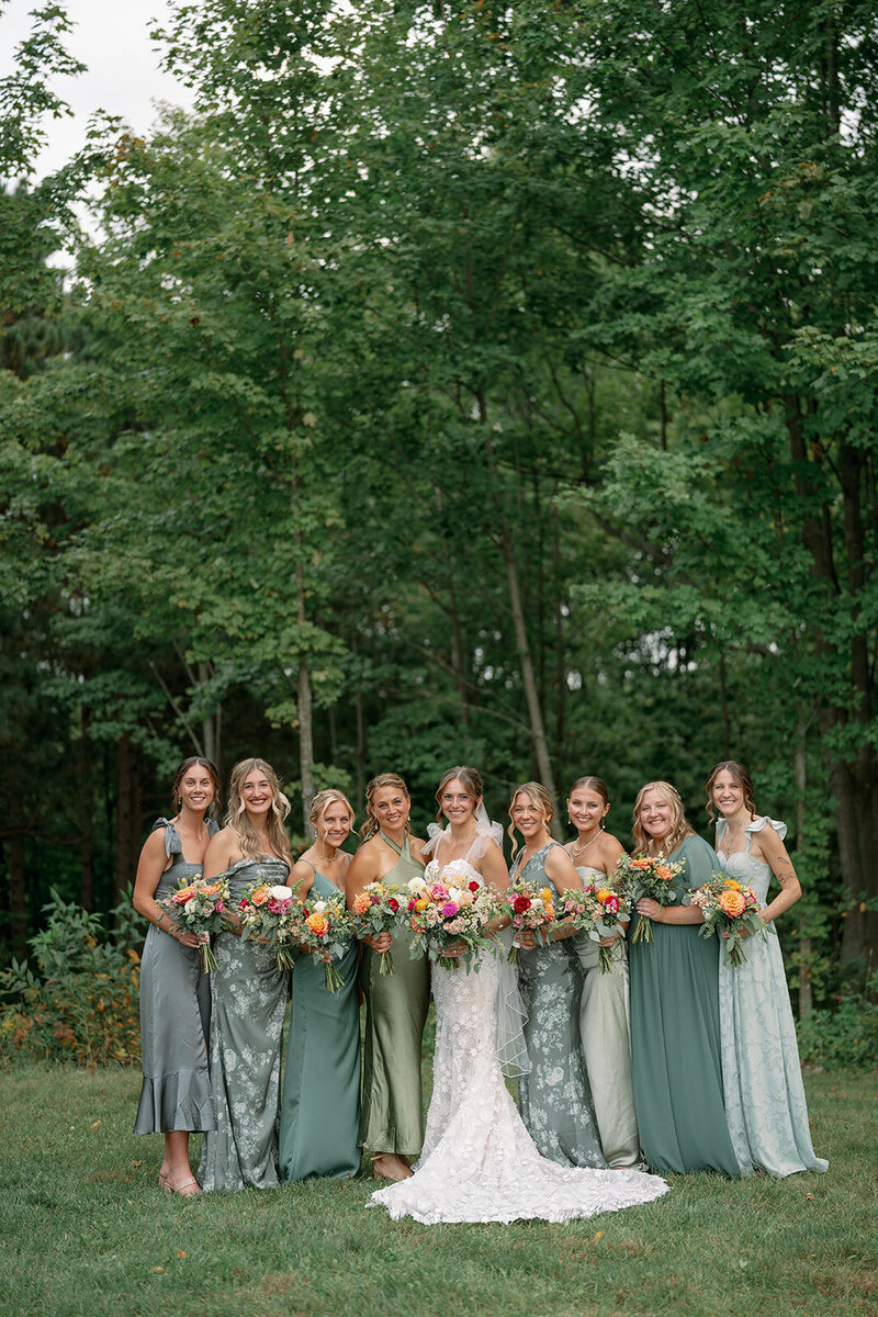 Bridesmaids wearing mixed green solid and floral dresses with bouquets, standing with the bride at The Cherry Barn at Nugent Orchards.