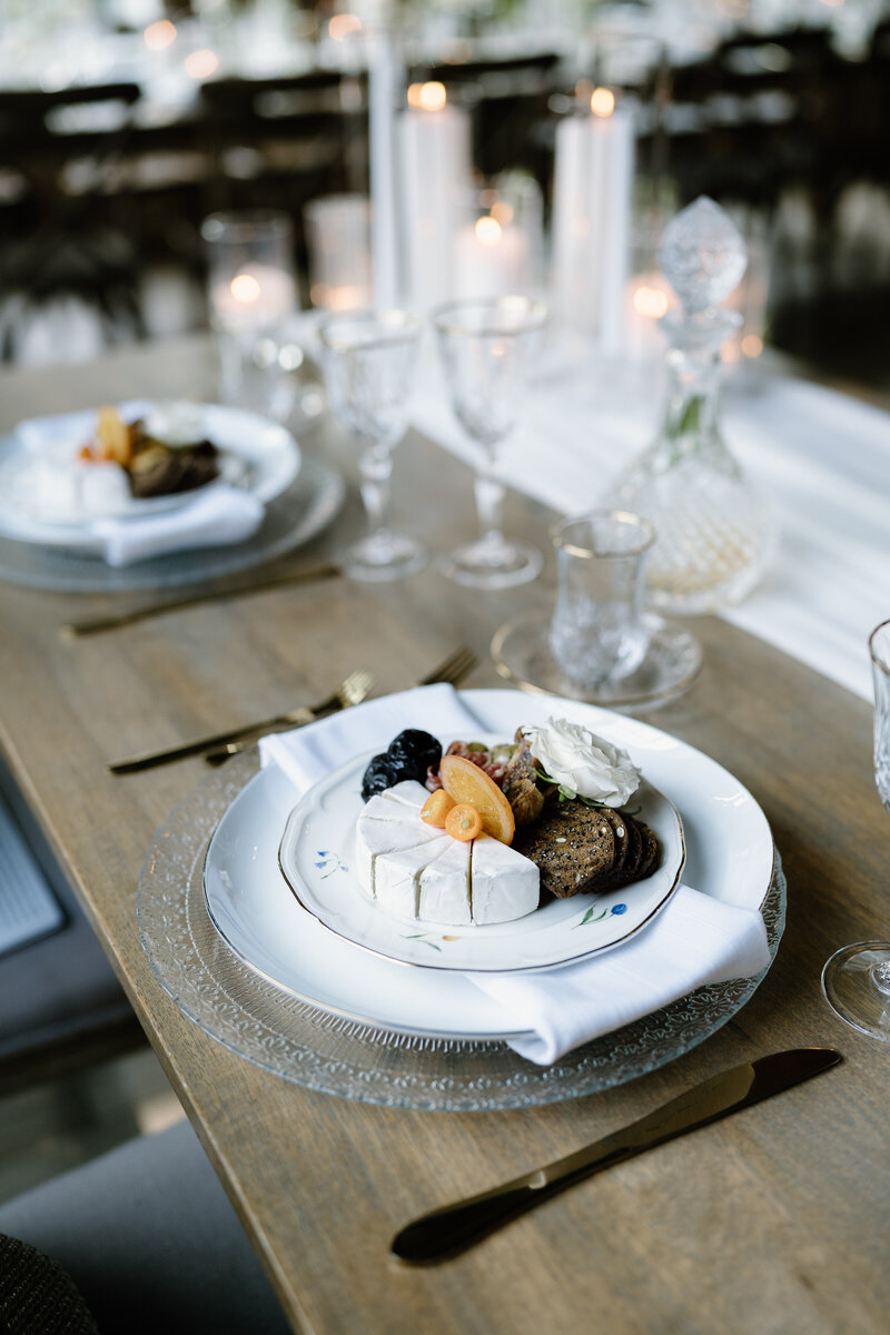 Charcuterie sits on timeless dishware surrounded by gold silverware, gold-rimmed glasses and white candles atop a wooden table at Chicago wedding.