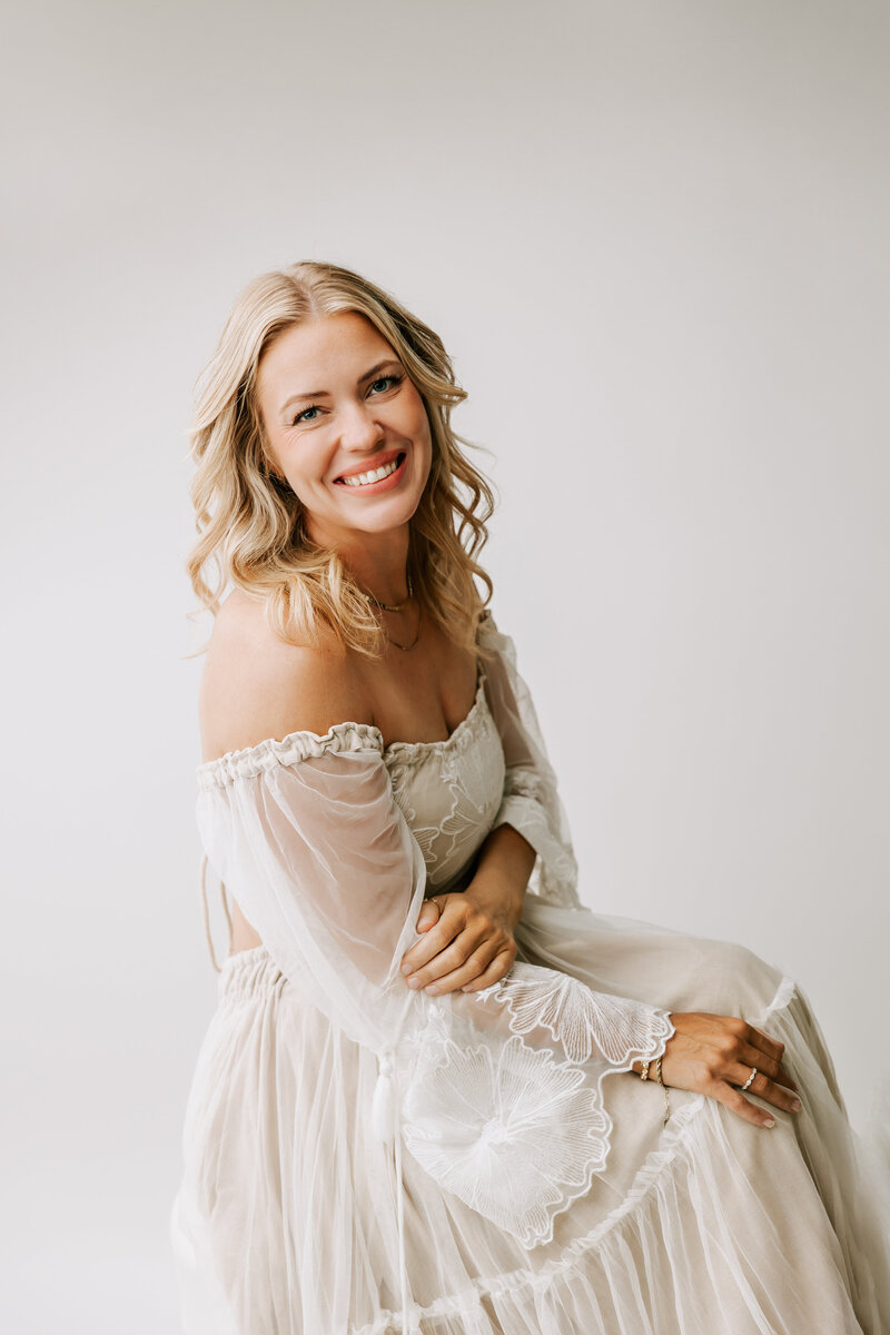 Fine art studio portland newborn photographer Ann Marshall in her portland oregon studio wearing white dress smiling at camera