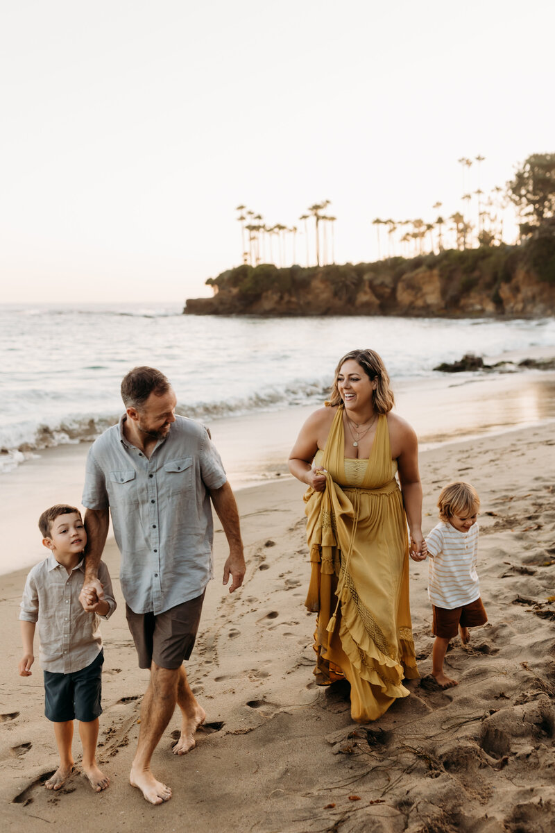Brittani Luce, a Southern California maternity and family photographer, walking along the beach with her husband and two sons during a golden-hour family session in Laguna Beach

