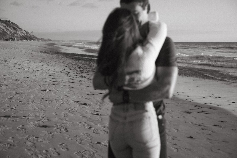 couple embraces on the beach for engagement photos in san diego