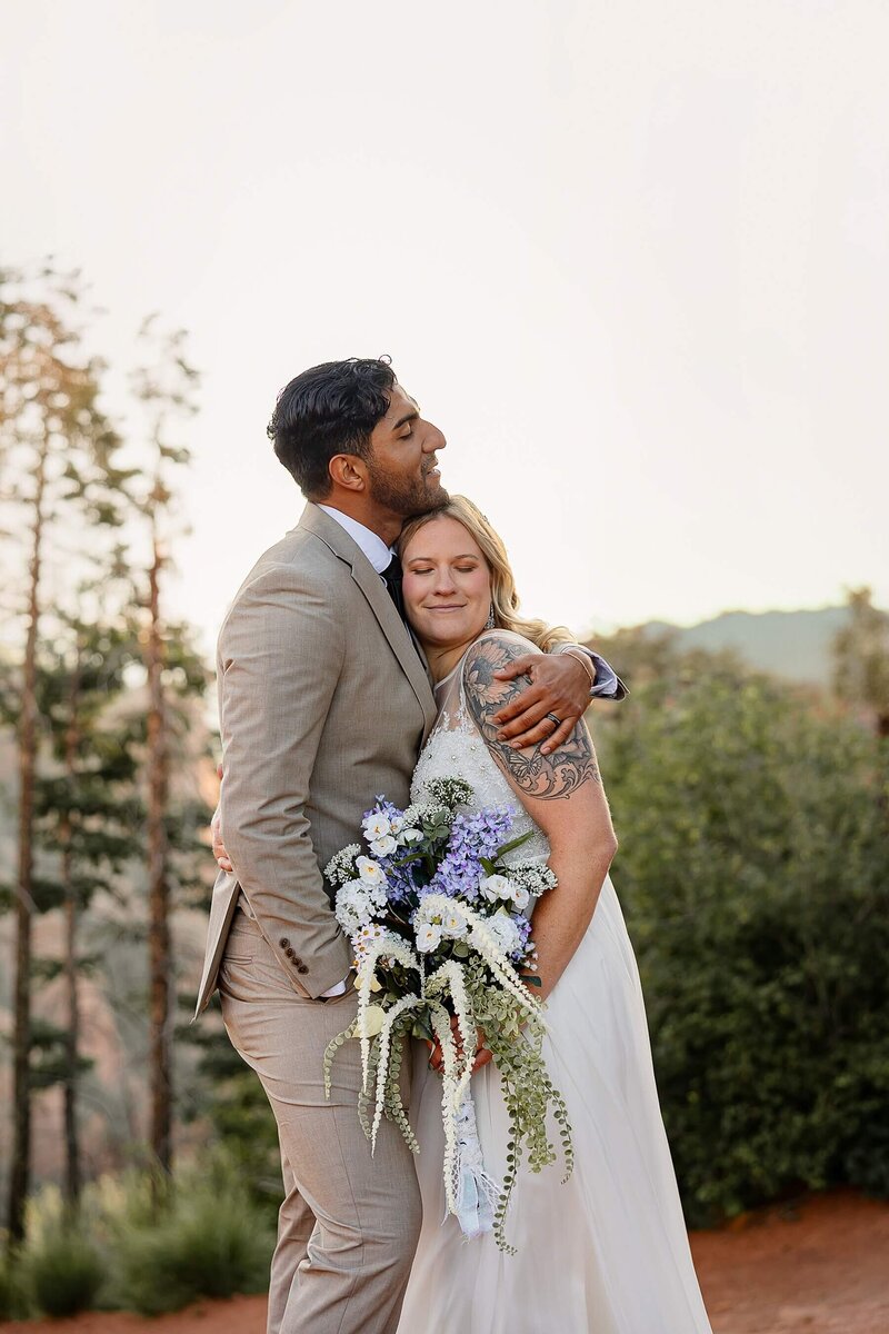 bride and groom snuggling with her bouquet and mountains in the background