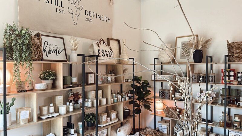 interior shot of The Still Refinery mercantile with stocked shelves full of skincare, pillows, candles and a pretty tree in the corner next to a warm lamp