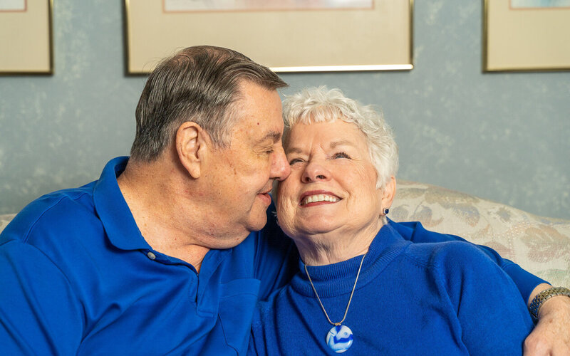A white couple dressed in blue shirts cuddle next to each other on the couch