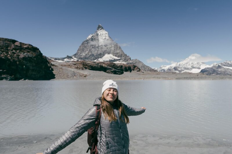 The girl is smiling while standing in front of the mountain