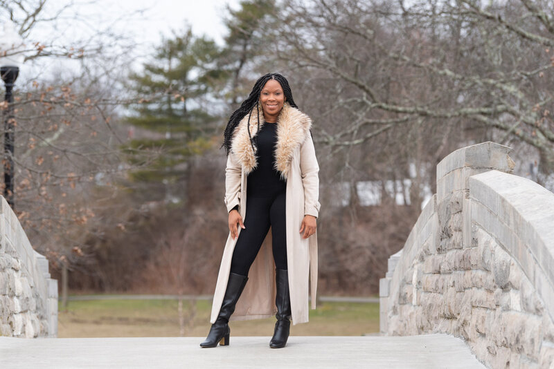 An African American woman standing on the bridge at a park posing and smiling for her outdoor headshot.
