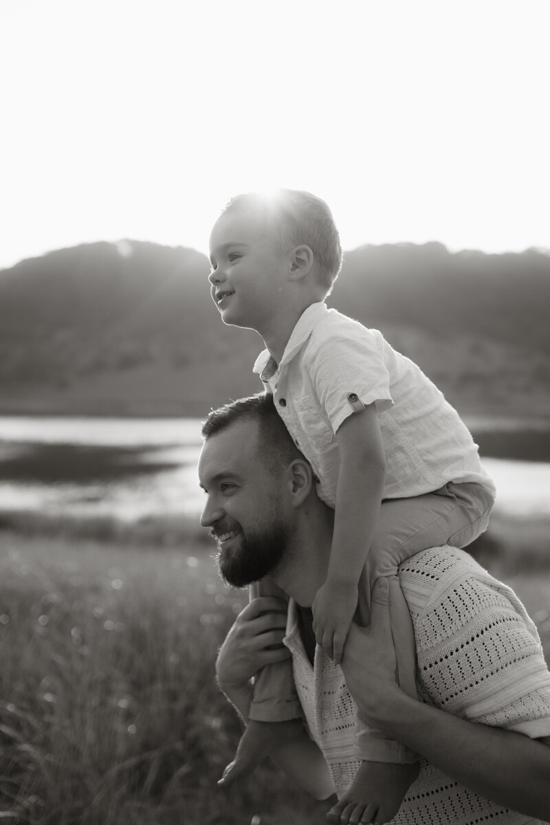 Black and white photo of Stephen from Rainstorm Photo & Video giving his son a piggyback ride at the dunes, captured in a joyful, cinematic light.