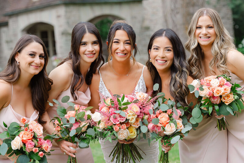 a bride and her bridesmaids in pink dresses holding pink bouquets and everyone is smiling happily.  Taken outdoors by Ottawa wedding photographer JEMMAN Photography