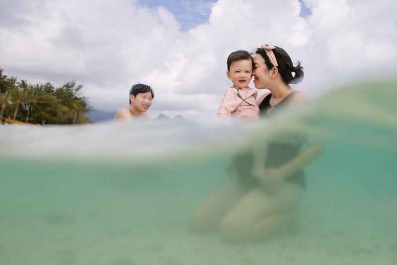 Blue, a man and woman play in the ocean as they hold a baby.