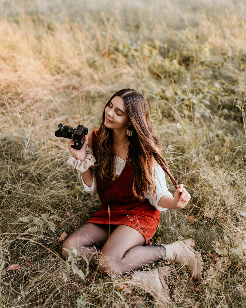 woman sitting in a field holding a camera while smiling