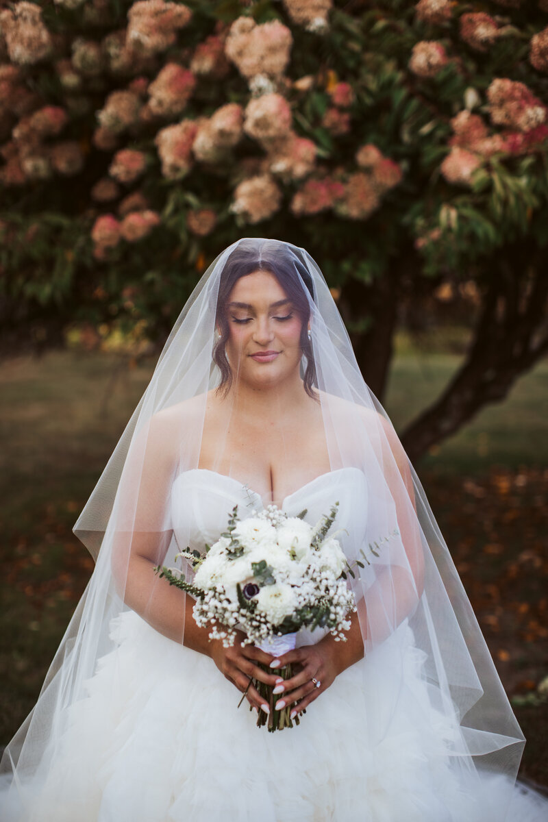 Bride in a long veil and gown smiling in a garden setting captured during her Maine wedding.