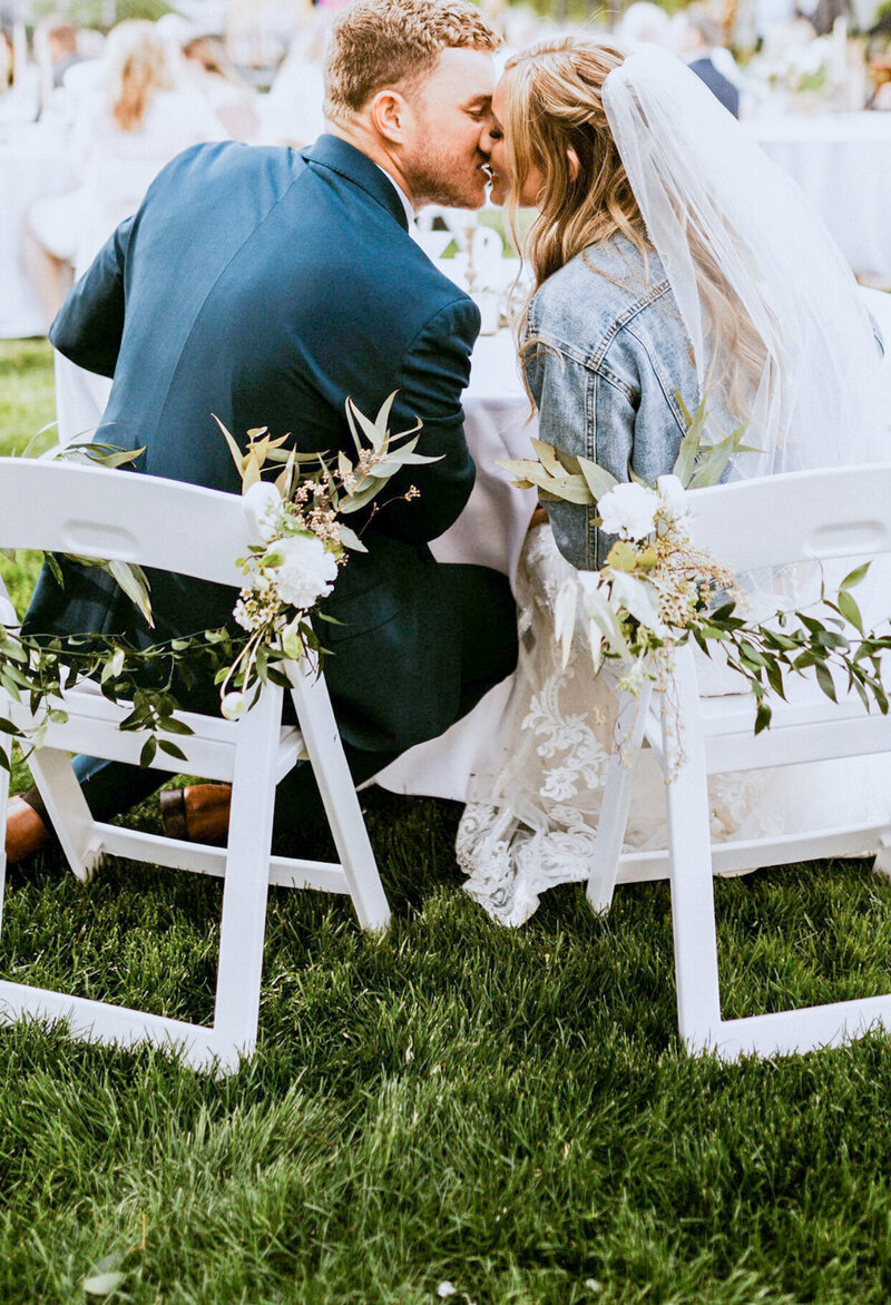 Couple sharing a kiss during their outdoor reception at the table.
