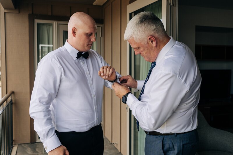 a groom in white shirt and black bowtie has cufflinks done by father in candid wedding morning moment at terrace downs