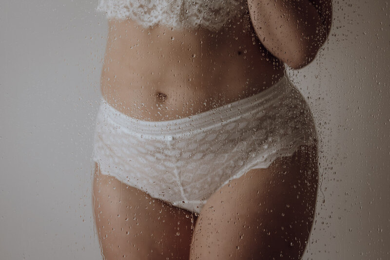 Close-up van een bruid die haar slip draagt, een zacht detail van lingerie en huid, gefotografeerd in natuurlijk licht.

