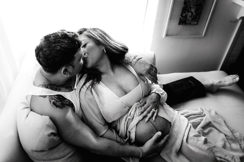 black and white photo of couple kissing and holding womans pregnant stomach
