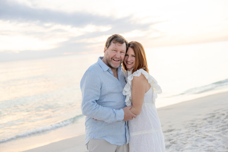 A couple standing close together at the beach smiling.