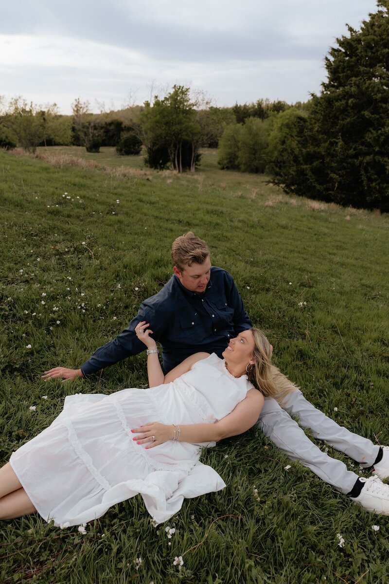 couple lays in field for engagement photos in texas