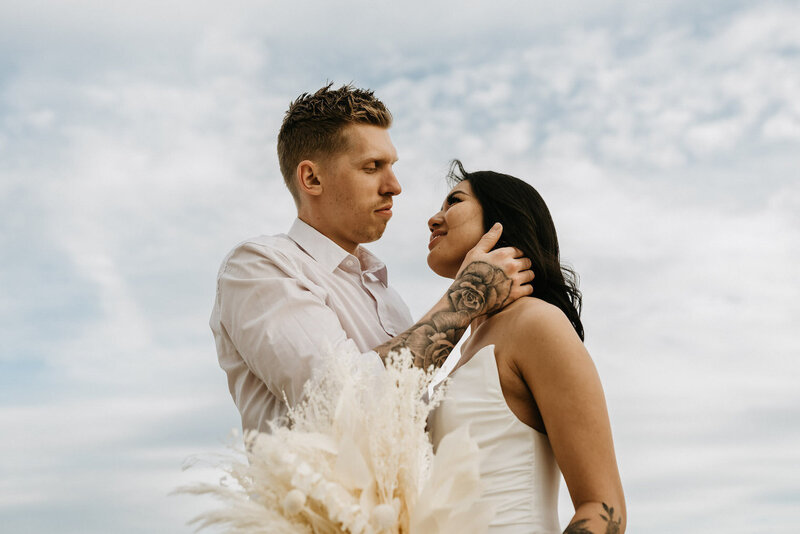 Modern wedding couple with cloudy sky behind them.