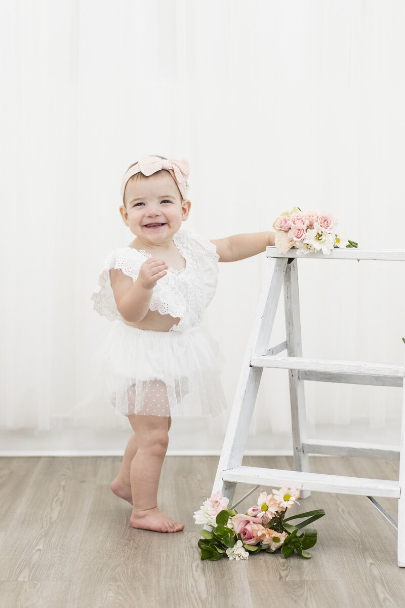 Photo of one year old girl standing by ladder smiling