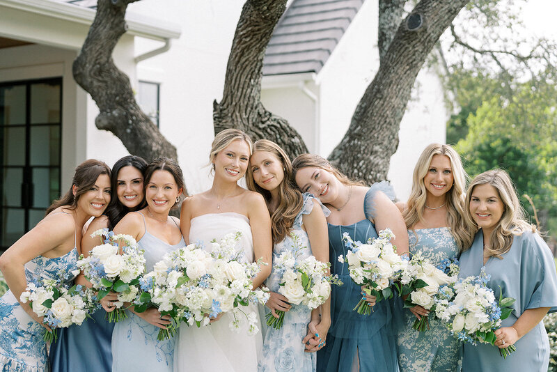 Bridesmaids in blue bridesmaid dresses, standing in front of The Arlo trees.