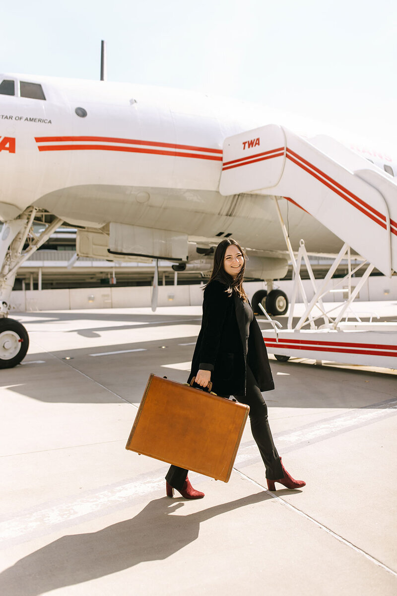 woman with suitcase and camera sits on tarmac stairs