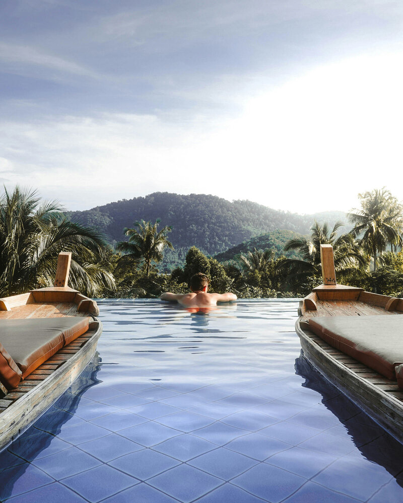 Man swimming in an infinity pool with mountains in the background