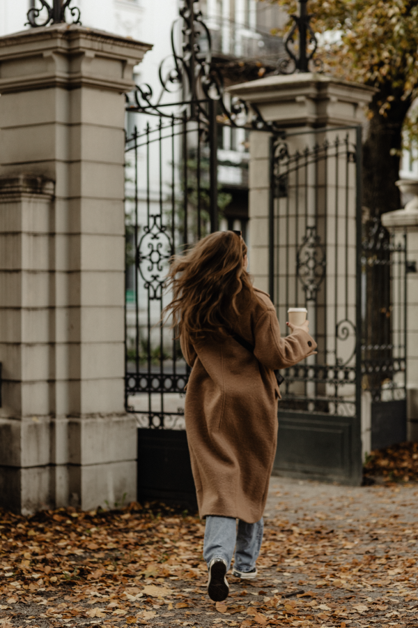 Aesthetic image of young woman in brown coat walking towards attractive iron gates | Brand By Design
