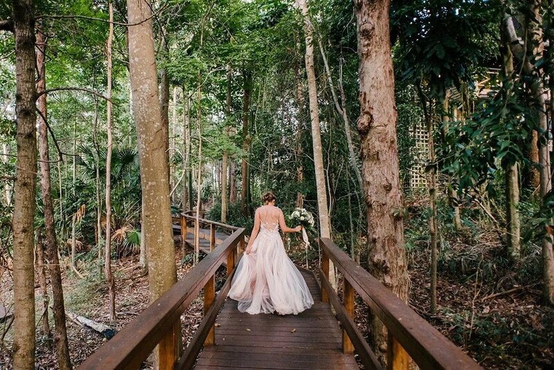 A bride walking away from the camera along a boardwork in a forest