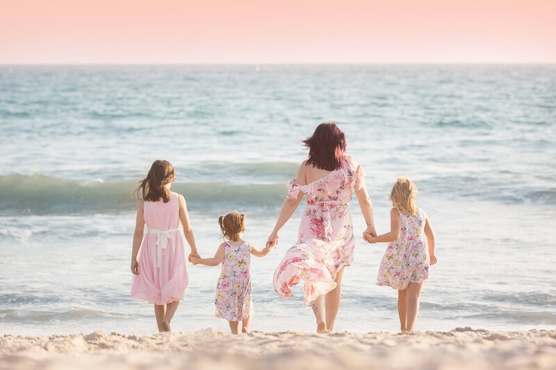 Mom with her three daughters at the beach in Santa Monica holding hands and walking towards the water