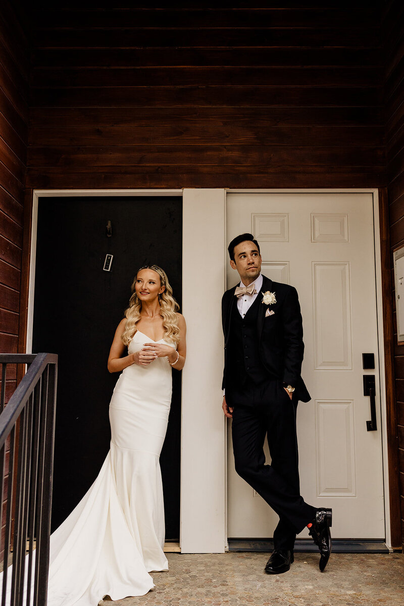 Bride and groom stand in front of doors looking in opposite directions before first look at elegant Chicago wedding.